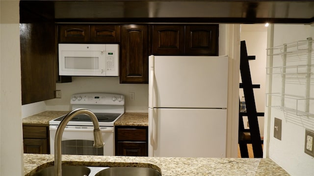 kitchen with dark brown cabinets, light stone counters, and white appliances