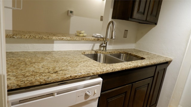 kitchen featuring dark brown cabinetry, light stone counters, stainless steel dishwasher, and sink