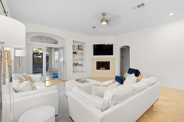 living room featuring ceiling fan, a fireplace, and built in shelves