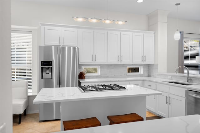 kitchen featuring a kitchen bar, hanging light fixtures, white cabinets, sink, and stainless steel appliances