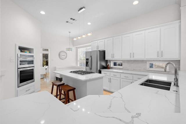 kitchen featuring white cabinets, a kitchen island, decorative light fixtures, stainless steel appliances, and sink