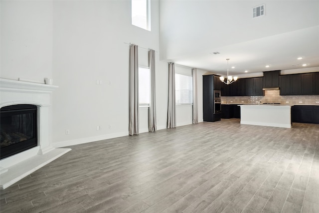 unfurnished living room with light hardwood / wood-style flooring, a chandelier, and a high ceiling