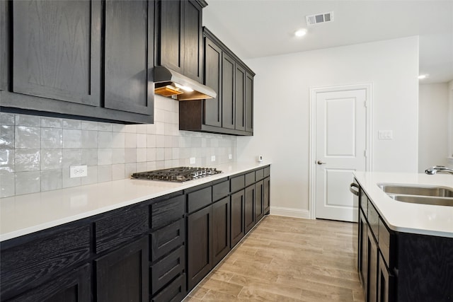 kitchen with stainless steel gas stovetop, sink, light wood-type flooring, and decorative backsplash