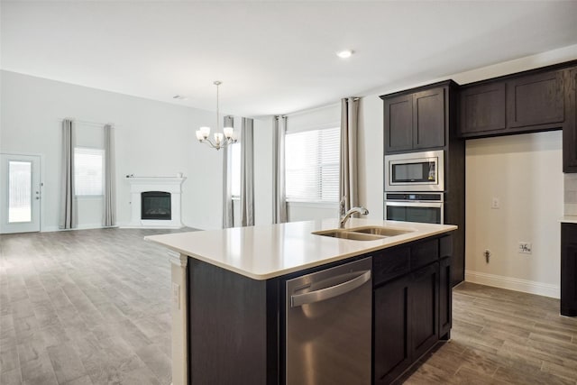 kitchen featuring sink, appliances with stainless steel finishes, a kitchen island with sink, hanging light fixtures, and dark brown cabinets