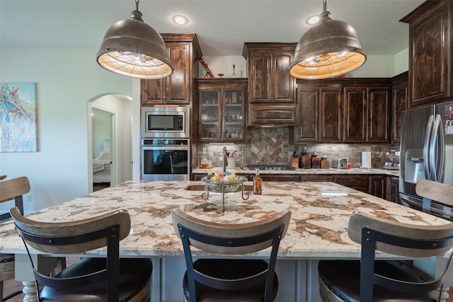 kitchen featuring hanging light fixtures, dark brown cabinets, stainless steel appliances, and a large island with sink