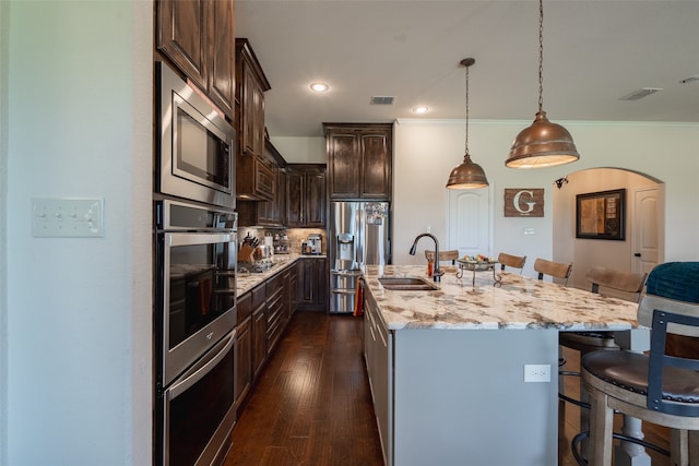 kitchen with sink, a breakfast bar area, appliances with stainless steel finishes, hanging light fixtures, and a center island with sink