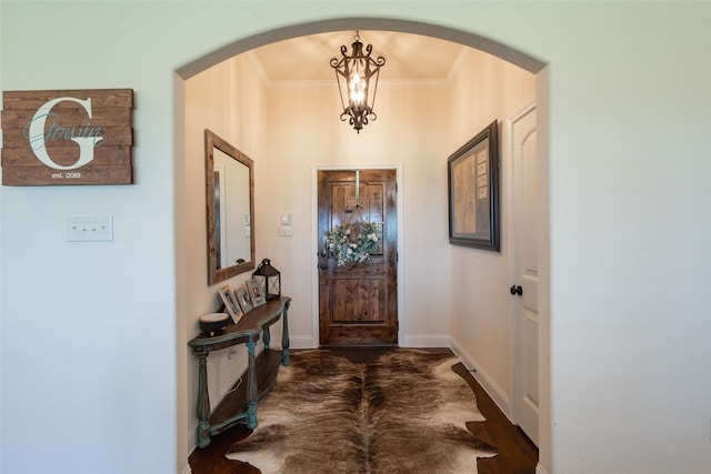 foyer entrance with dark wood-type flooring, ornamental molding, and a notable chandelier