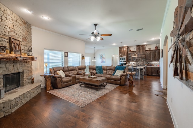 living room featuring crown molding, a stone fireplace, dark hardwood / wood-style floors, and ceiling fan