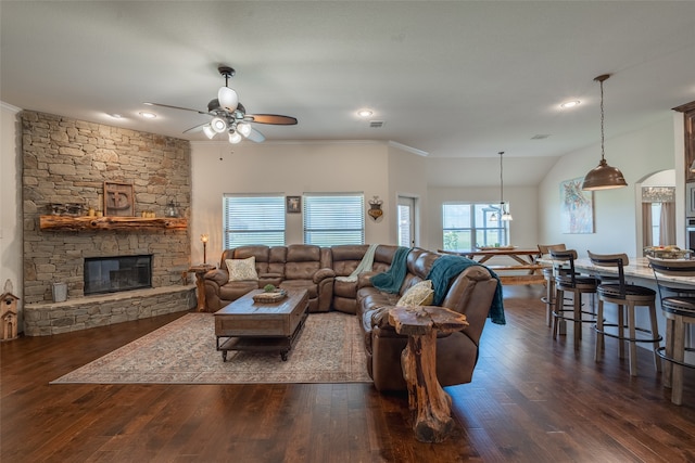 living room featuring dark hardwood / wood-style flooring, a stone fireplace, crown molding, and ceiling fan