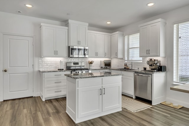 kitchen with a kitchen island, hardwood / wood-style floors, white cabinets, stainless steel appliances, and light stone countertops