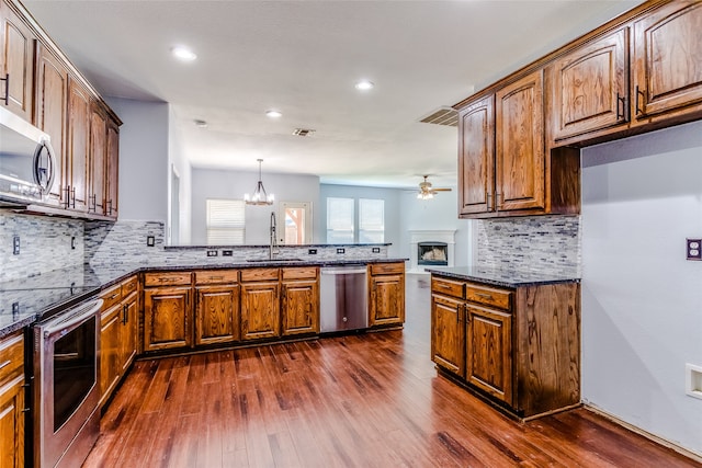 kitchen featuring sink, stainless steel appliances, dark hardwood / wood-style floors, pendant lighting, and ceiling fan with notable chandelier