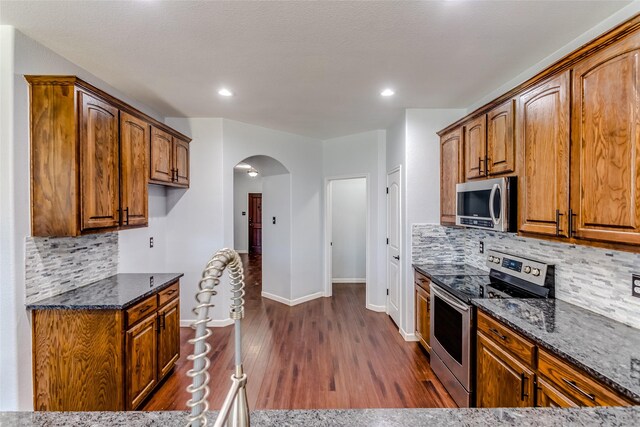 kitchen with tasteful backsplash, stainless steel appliances, dark stone counters, and dark wood-type flooring