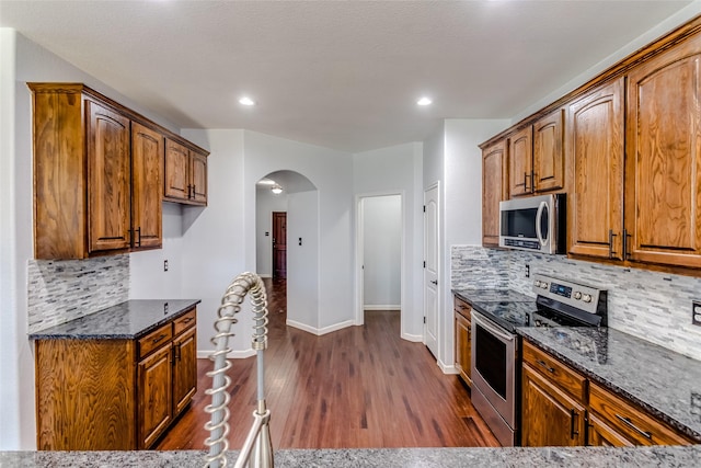 kitchen with appliances with stainless steel finishes, dark stone countertops, backsplash, and dark hardwood / wood-style flooring