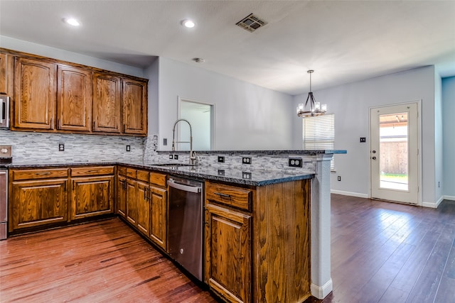 kitchen featuring a notable chandelier, kitchen peninsula, hardwood / wood-style floors, dark stone counters, and appliances with stainless steel finishes