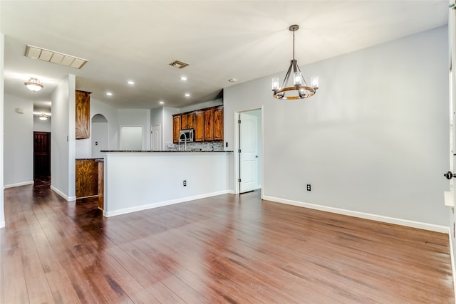 kitchen featuring backsplash, pendant lighting, wood-type flooring, and a notable chandelier