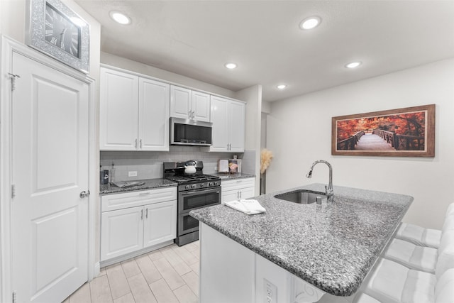 kitchen featuring white cabinetry, sink, dark stone counters, a breakfast bar area, and appliances with stainless steel finishes