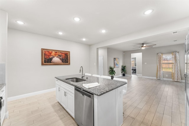 kitchen featuring sink, dark stone countertops, dishwasher, white cabinetry, and an island with sink