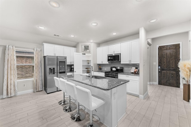 kitchen featuring sink, stainless steel appliances, an island with sink, dark stone counters, and white cabinets