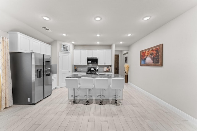 kitchen featuring a kitchen breakfast bar, dark stone countertops, an island with sink, appliances with stainless steel finishes, and white cabinetry