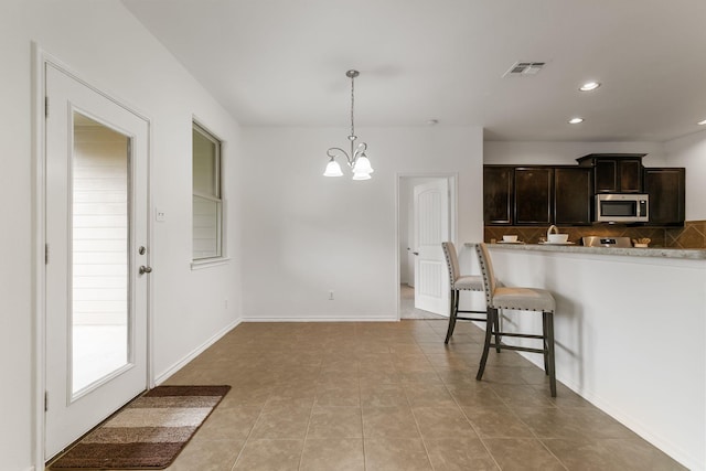 kitchen with decorative light fixtures, a chandelier, a breakfast bar, light tile patterned floors, and dark brown cabinets