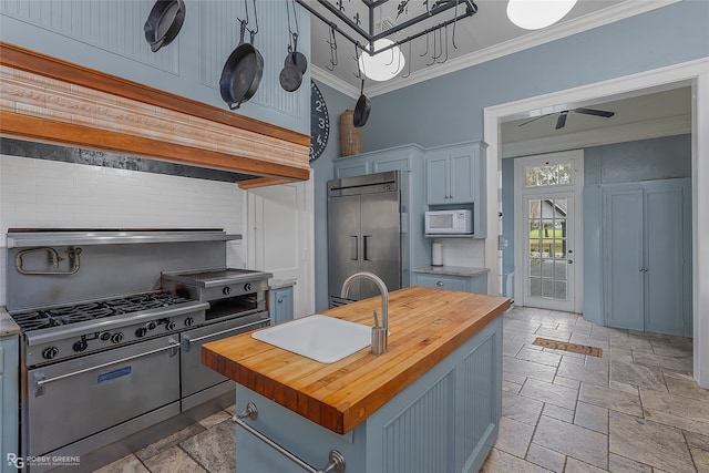 kitchen featuring wood counters, stainless steel built in refrigerator, blue cabinets, a center island with sink, and ornamental molding