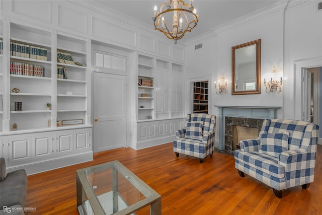 sitting room with built in features, a chandelier, wood-type flooring, a fireplace, and ornamental molding