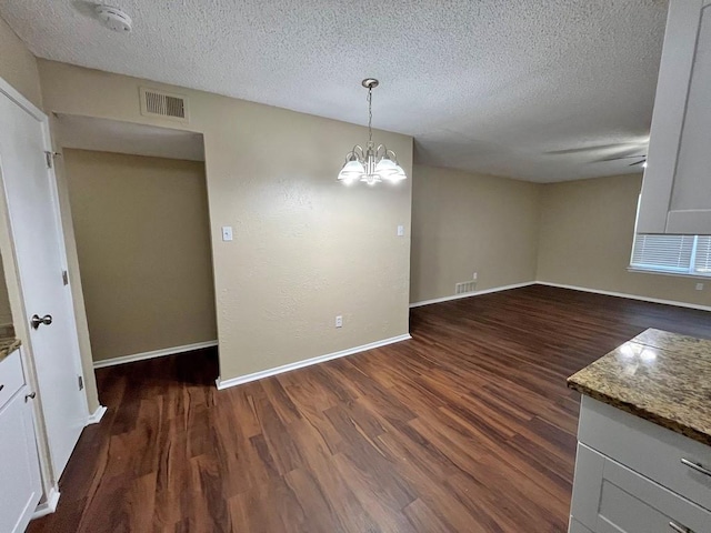 unfurnished dining area with an inviting chandelier, dark wood-type flooring, and a textured ceiling