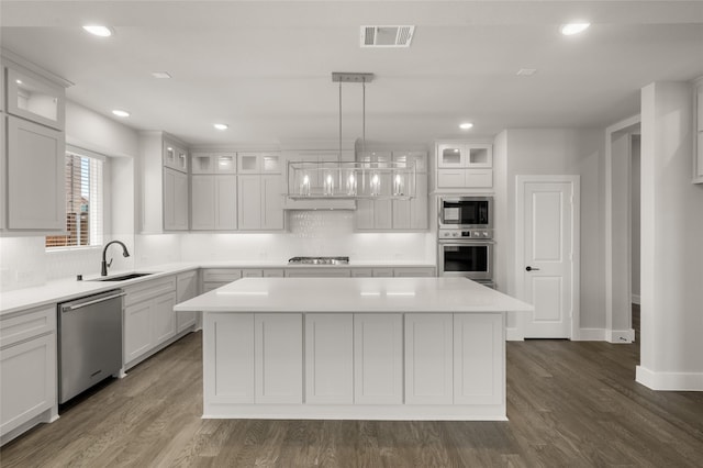 kitchen with appliances with stainless steel finishes, a sink, light countertops, a center island, and backsplash