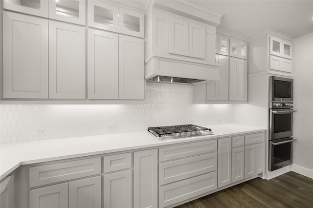 kitchen with tasteful backsplash, light countertops, stainless steel appliances, dark wood-type flooring, and glass insert cabinets