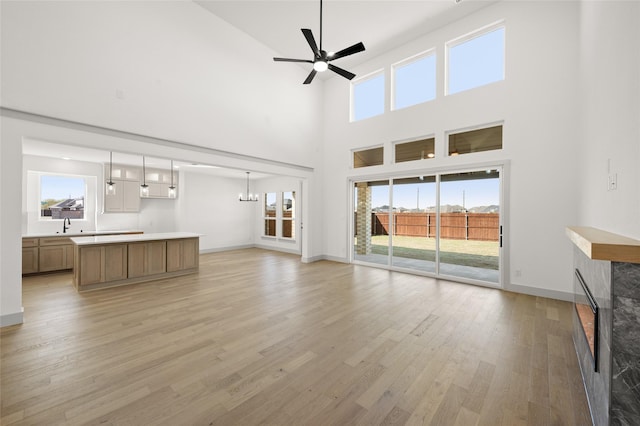 unfurnished living room featuring a high ceiling, ceiling fan, plenty of natural light, and light wood-style floors