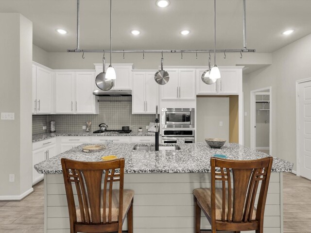 kitchen with decorative light fixtures, appliances with stainless steel finishes, and a center island with sink