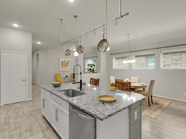 kitchen with light stone countertops, white cabinets, dishwasher, an island with sink, and sink