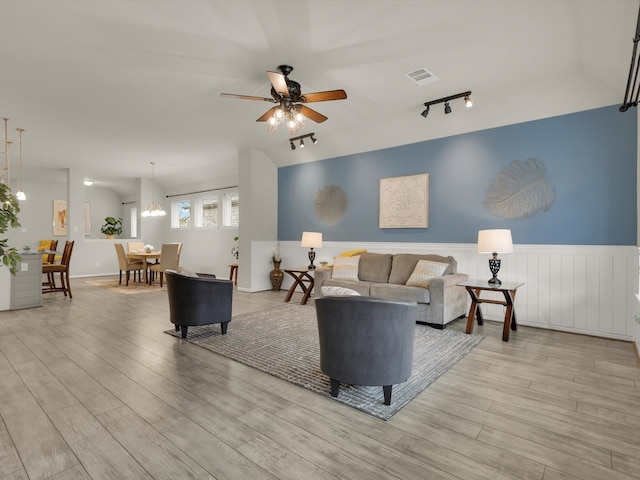 living room with ceiling fan with notable chandelier, track lighting, and light wood-type flooring