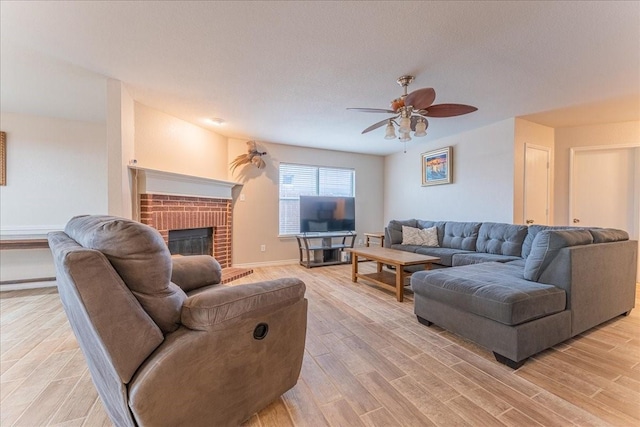 living room with ceiling fan, a textured ceiling, a fireplace, and light hardwood / wood-style flooring