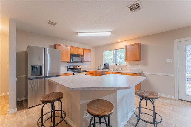 kitchen with sink, a breakfast bar area, light hardwood / wood-style flooring, appliances with stainless steel finishes, and a kitchen island