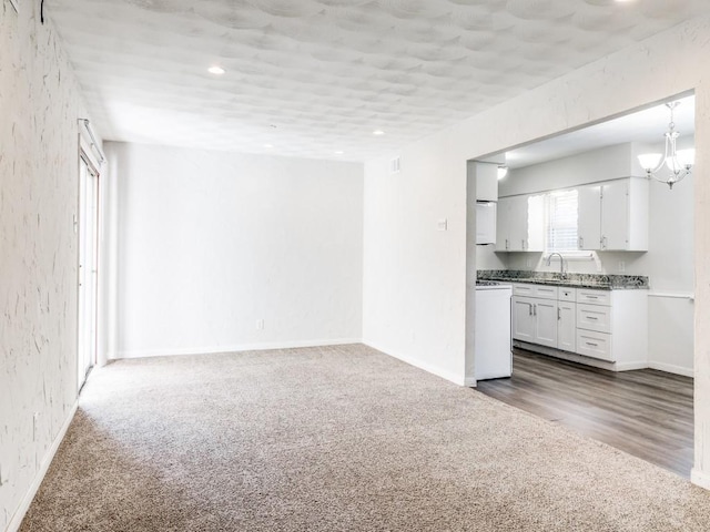 unfurnished living room featuring sink, a notable chandelier, and dark colored carpet