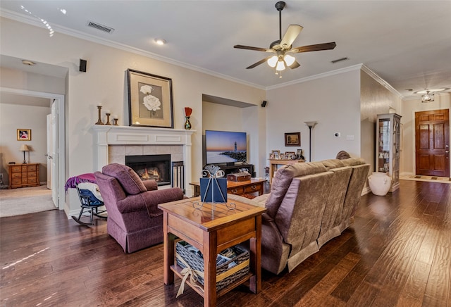 living room featuring a tile fireplace, ornamental molding, ceiling fan, and dark wood-type flooring