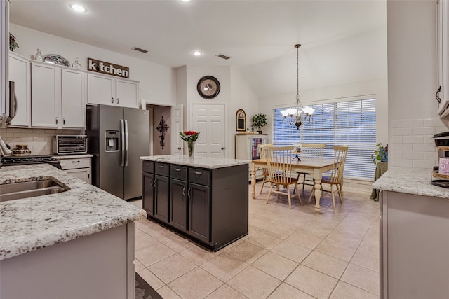 kitchen with a center island, stainless steel fridge with ice dispenser, light stone counters, vaulted ceiling, and decorative light fixtures