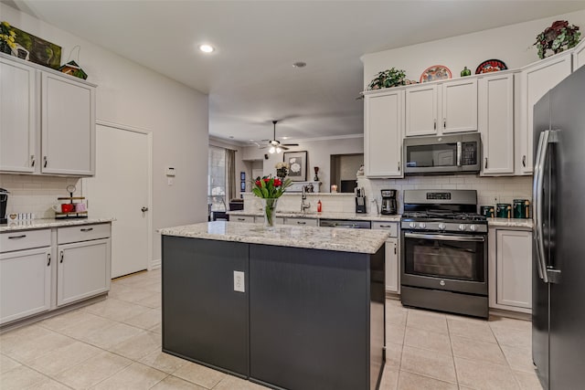 kitchen with light stone countertops, a kitchen island, stainless steel appliances, and ceiling fan