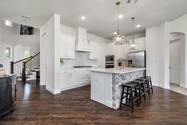 kitchen featuring white cabinets, premium range hood, a kitchen island with sink, and stainless steel appliances