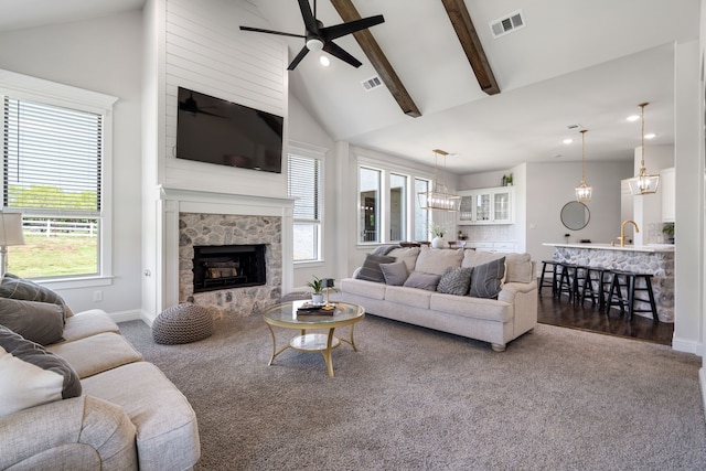 living room with dark wood-type flooring, beamed ceiling, high vaulted ceiling, a fireplace, and ceiling fan with notable chandelier