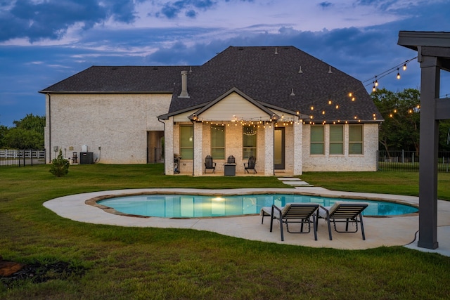 pool at dusk featuring a yard, central AC, and a patio area