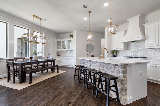 kitchen with premium range hood, dark wood-type flooring, a center island with sink, sink, and white cabinetry