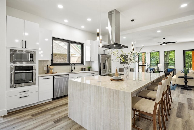 kitchen featuring appliances with stainless steel finishes, white cabinetry, hanging light fixtures, a center island, and island range hood