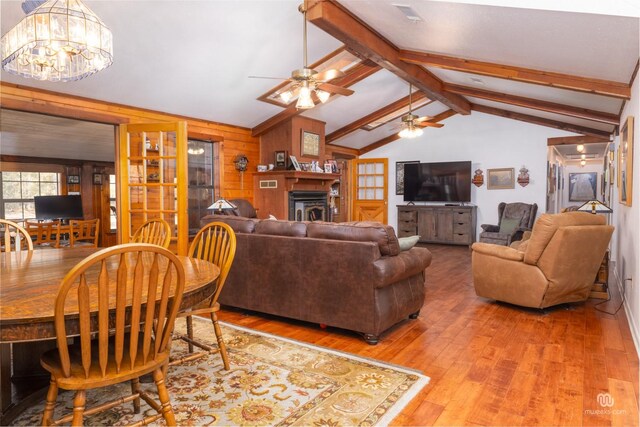 living room with ceiling fan with notable chandelier, hardwood / wood-style floors, vaulted ceiling with beams, and wooden walls