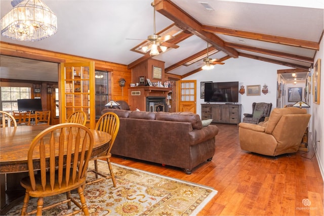 living room featuring hardwood / wood-style floors, ceiling fan with notable chandelier, vaulted ceiling with beams, and wood walls