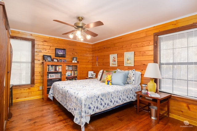 bedroom with ornamental molding, dark wood-type flooring, ceiling fan, and wood walls