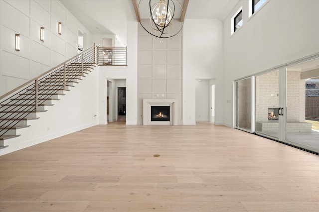 unfurnished living room featuring a large fireplace, an inviting chandelier, and light hardwood / wood-style floors