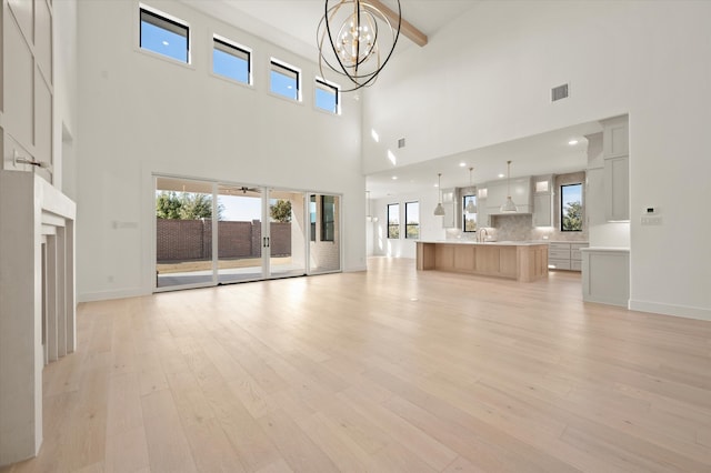 unfurnished living room featuring beamed ceiling, light wood-type flooring, a wealth of natural light, and an inviting chandelier