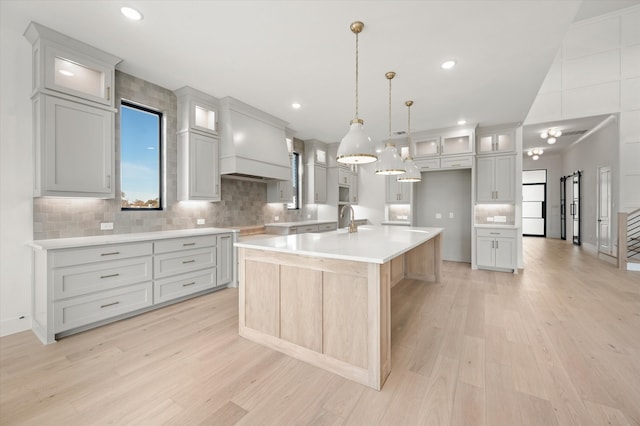 kitchen featuring a spacious island, decorative light fixtures, custom exhaust hood, and light wood-type flooring